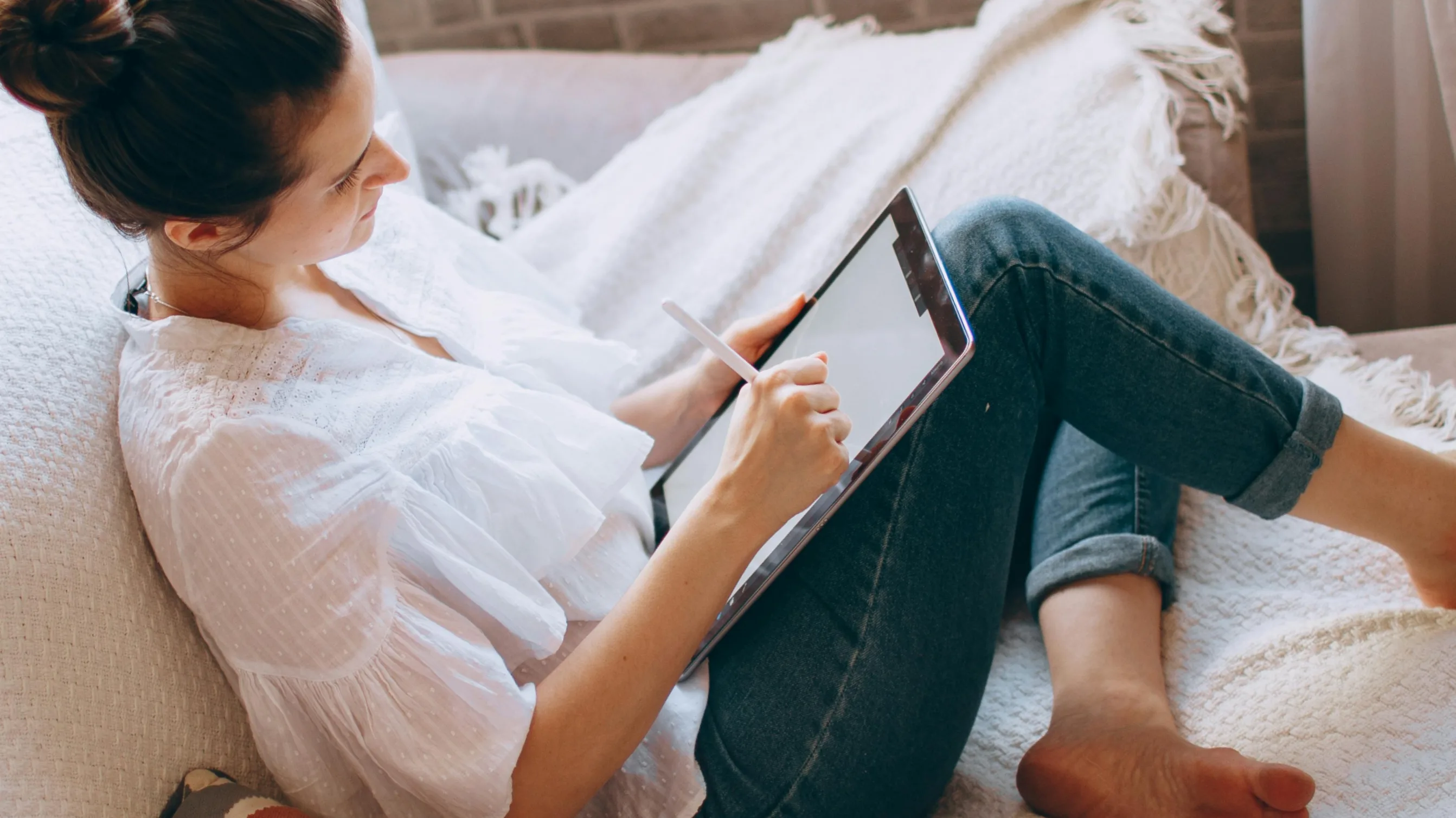 Eine Frau sitzt auf einem Sofa und schaut auf einen Tablet-Computer.