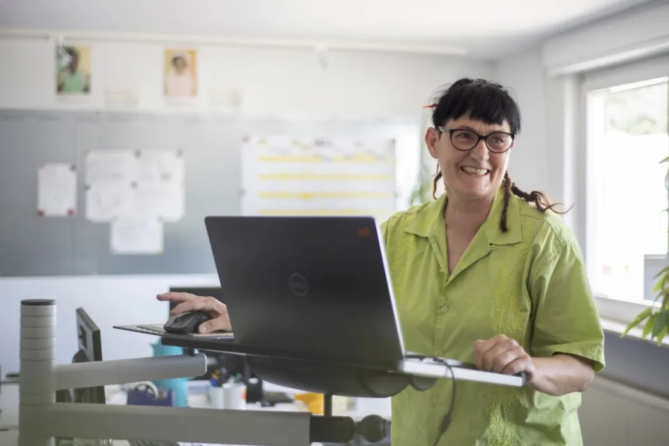 Eine Frau steht an einem Steh-Schreibtisch und arbeitet am Computer.